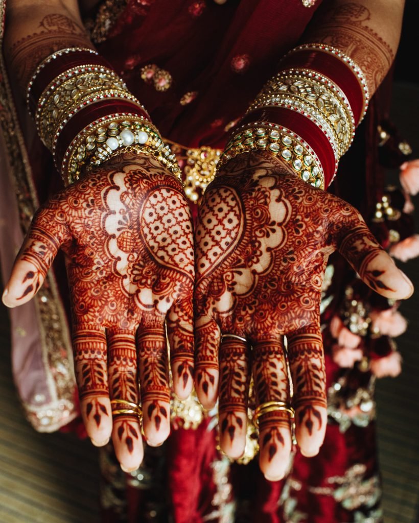 Traditional indian heart ornament on hands colored by henna and bridal bracelets in bordeaux colours